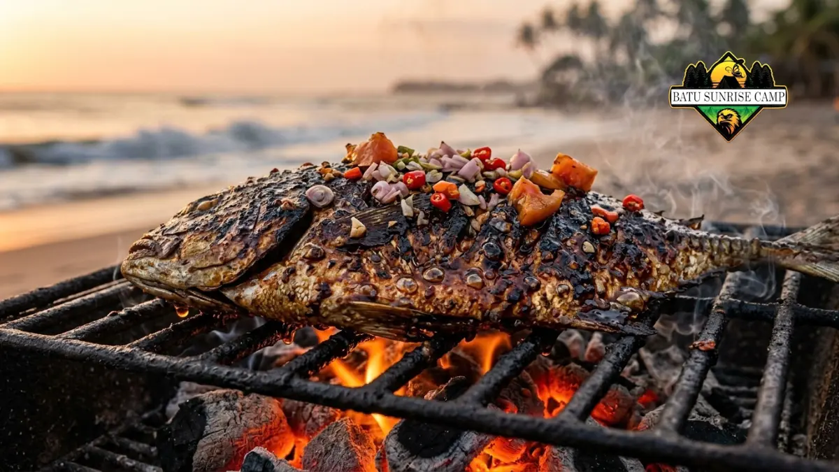 Ikan kembung bakar bumbu kecap manis di atas grill arang portable dengan olesan bumbu mengaramel di tepi pantai saat senja