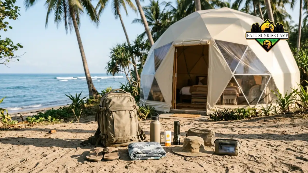 Perlengkapan menginap di glamping dome pantai tersusun rapi di atas tikar meliputi tabir surya, senter, obat pribadi, dan kantong sampah