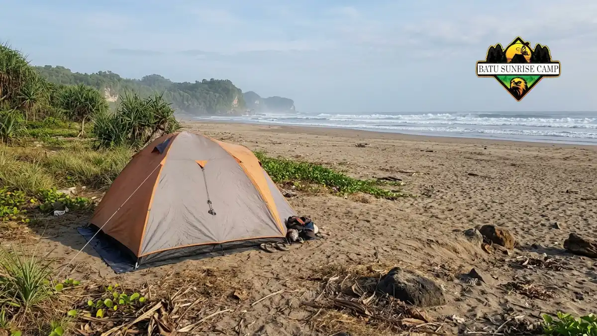 Tenda camping dome berdiri di area pasir pantai yang aman jauh dari garis pasang dengan ombak dan tebing di latar belakang