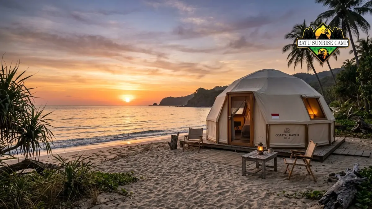 Tenda glamping dome putih di pantai pasir saat matahari terbenam dengan langit jingga keemasan dan kursi kayu di dek depan tenda